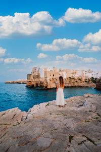 Woman standing on rock by sea against sky