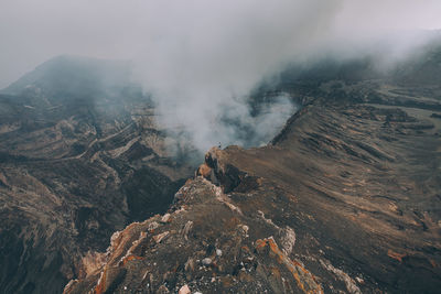 High angle view of woman standing by smoke emitting from volcanic crater
