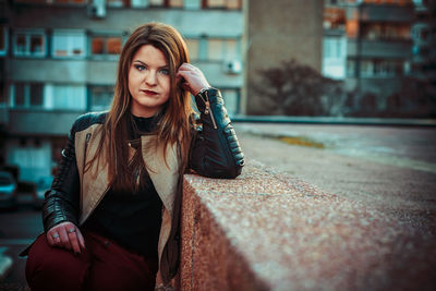 Portrait of young woman sitting against building