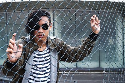 Portrait of young man looking through chainlink fence