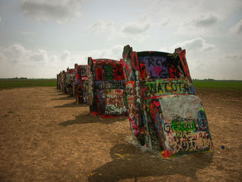 Graffiti on abandoned cars on field against sky
