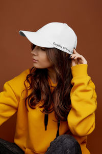 Portrait of young woman wearing hat against wall