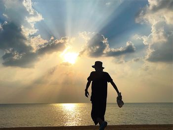 Rear view of silhouette mature man standing at beach against sky during sunset
