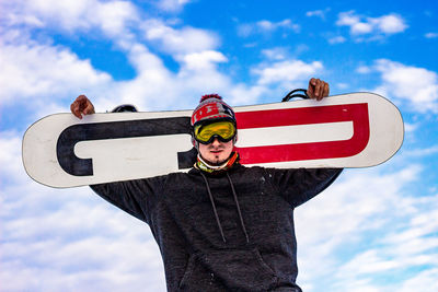 Low angle view of man standing against sky with snowboard 