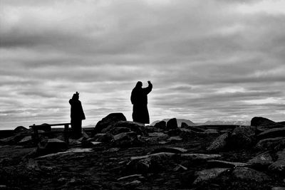 Rear view of people sitting on rock against cloudy sky