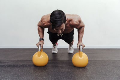 Male athlete doing push-ups on yellow kettlebell in gym