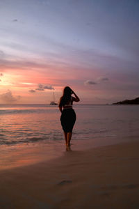 Silhouette woman standing at beach against sky during sunset