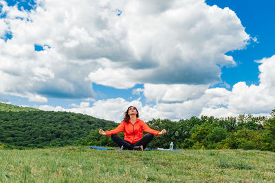 Side view of woman sitting on grassy field against sky