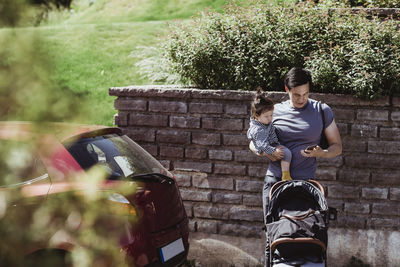 Father using smart phone while carrying baby son on sunny day