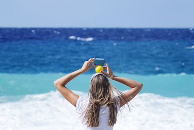 Rear view of woman holding toys on beach against clear sky