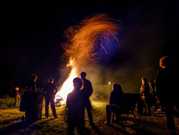 People standing around bonfire against sky at night