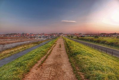 Road amidst grass against sky during sunset