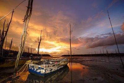 Sailboats moored at harbor against cloudy sky during sunset