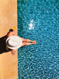 High angle view of woman wearing hat sitting at poolside during sunny day