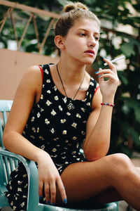 Thoughtful woman holding cigarette while sitting on chair