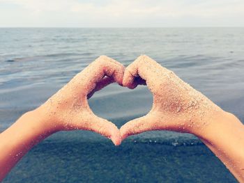 Close-up of hands making heart shape against sea