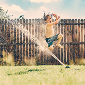 Boy jumping through a sprinkler in back yard