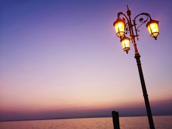 Street light by sea against sky during sunset