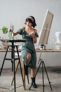 Full length of painter sitting on stool by easel at art studio