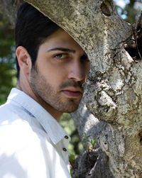 Close-up portrait of young man against tree trunk