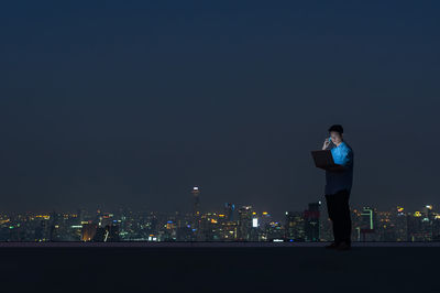 Man standing by illuminated buildings against sky at night