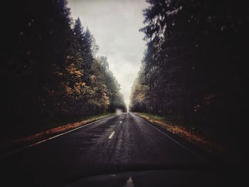 Road amidst trees against sky seen through car windshield