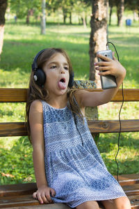 Smiling girl listening music while sitting on bench at park