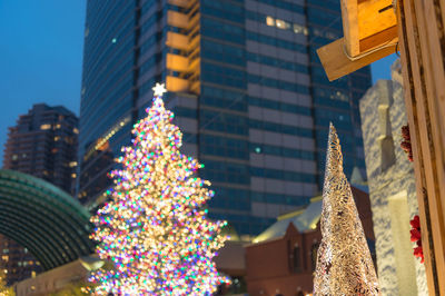 Low angle view of illuminated christmas tree against buildings in city