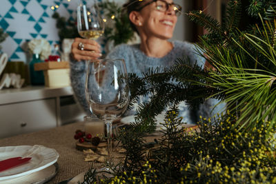 Smiling woman drinking wine sitting by christmas tree at home