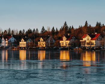 Houses by lake and buildings against clear sky