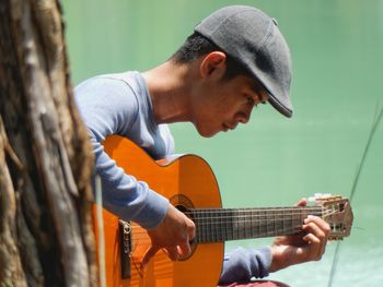 Side view of young man playing acoustic guitar against lake