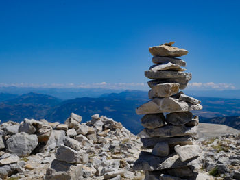 Stack of stones on rocks by sea against blue sky