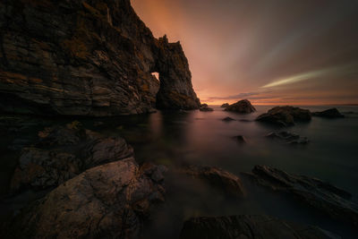 Rock formation on sea against sky during sunset