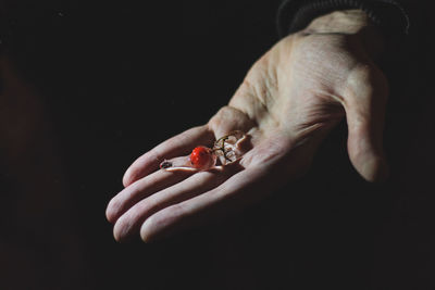 Cropped image of person holding frozen berry against black background