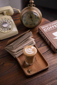 High angle view of coffee by book with clock and telephone on table