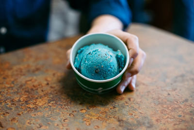 Close-up of person holding ice cream cup on rusty metallic table at cafe