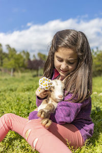 Smiling girl playing with kid goat on grassy land