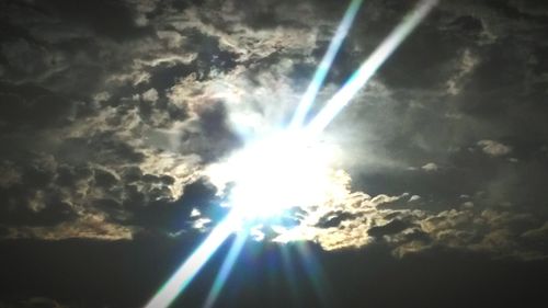 Low angle view of sun shining through clouds