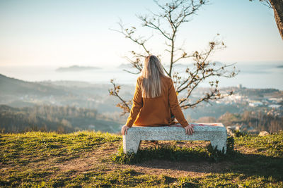 Rear view of woman sitting on bench against sky