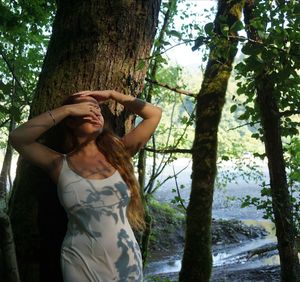 Young woman standing by tree trunk in forest