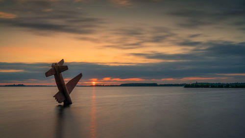 Silhouette person in sea against sky during sunset