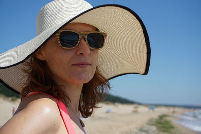 Portrait of woman wearing sunglasses and hat at beach against sky