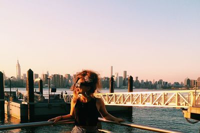 Smiling young woman standing by railing against river and bridge