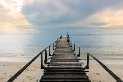 Pier on beach against sky during sunset