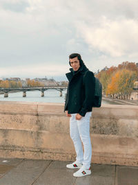 Full length portrait of man standing on bridge over river against sky