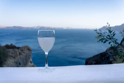 Close up of an ouzo stemmed glass on a white stand during sunset with the santorini caldera