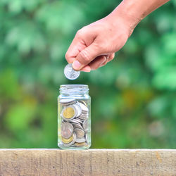 Cropped hand putting coin in jar on table