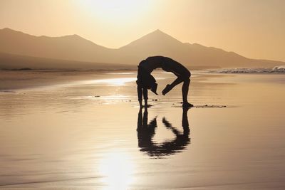 Silhouette of woman exercising at beach during sunset