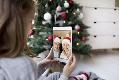 Girl video conferencing while holding digital tablet by christmas tree