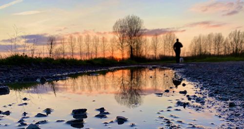 Silhouette person standing by lake against sky during sunset